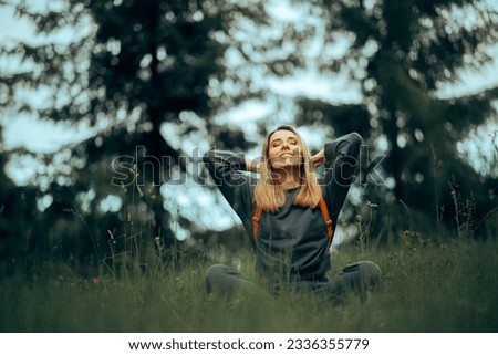 
Happy Millennial Woman Relaxing in the Grass Enjoying Nature. Carefree adult girl feeling disconnected from stress and urban life 
