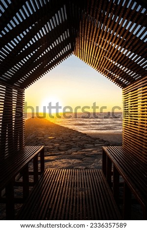 sunset on a beach with a rocky pier and waves at sea, sunset framed by a wooden bench construction