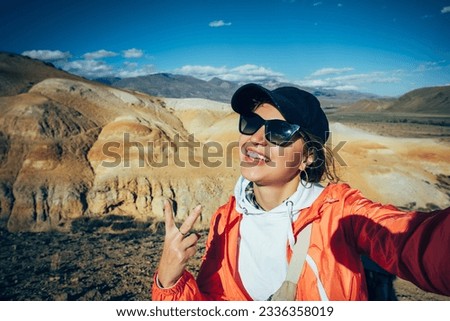 Cheerful woman tourist take a selfie with amazing mountain view. Happy young brunette enjoying vacation. Female traveller portrait.