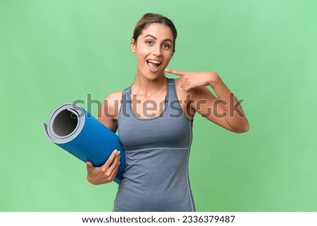 Pretty Young Uruguayan sport woman going to yoga classes while holding a mat over isolated background giving a thumbs up gesture
