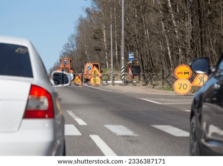 Road signs for speed limits, repairs and narrowing of the road. Traffic on the suburban highway. Blurred silhouettes of vehicles in the foreground.