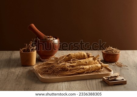 Ginseng roots and medicine herbs on wooden tray decorated with wooden mortar and pestle on brown background. Herbal for the preparation of a tonic drink. Photography traditional medicine content
