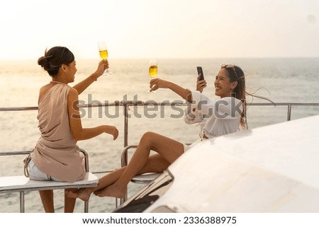 Young Asian woman friends using digital smartphone taking picture together during travel ocean on luxury private catamaran boat yacht sailing in the sea on summer holiday vacation at tropical island.