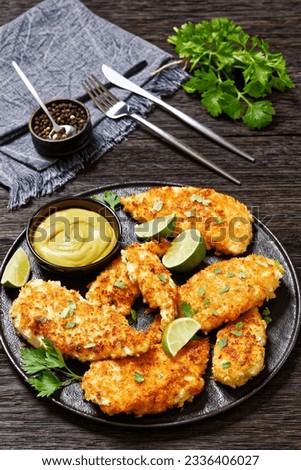 fried chicken cutlets under breadcrumbs and parmesan cheese crust on black plate with mustard and lime on dark wooden table, close-up, vertical view Royalty-Free Stock Photo #2336406027