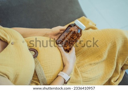Prenatal Vitamins. Portrait Of Beautiful Smiling Pregnant Woman Holding Transparent Glass Jar With Pills, Taking Supplements For Healthy Pregnancy While Sitting On Couch At Home, Free Space Royalty-Free Stock Photo #2336410957