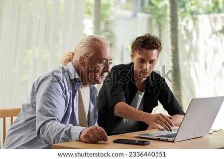 Senior man asking teenage grandson to help him with paying for online service Royalty-Free Stock Photo #2336440551