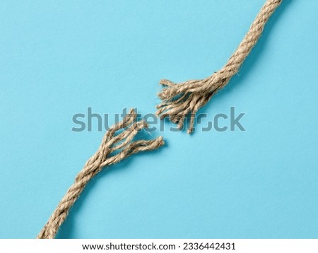 Separation, disconnection, failure or risk concepts. Frayed and broken rope torn apart into two pieces on blue background with copy space. Royalty-Free Stock Photo #2336442431