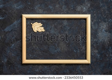 Wooden frame and wooden tree leave on dark blue concrete wall. Fall, autumn holidays concept. Flat lay, top view, copy space