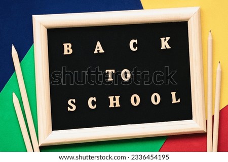 Back to school text, wooden letters in black background, frame on colored paper sheets, pencils. Concept of education, starting school. Colorful background