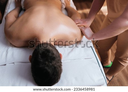 Closeup top view of unrecognizable muscular man getting massage comfortably lying on massage table in spa salon. Massage therapist massages client hands pressing, glides over hand to disperse lymph. Royalty-Free Stock Photo #2336458981