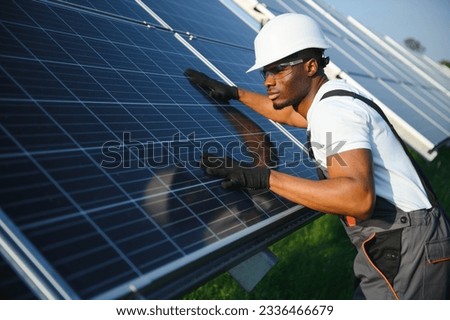 African American engineer maintaining solar cell panels. Technician working outdoor on ecological solar farm construction. Renewable clean energy technology concept.