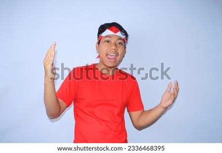 portrait of excited indonesian man show gesture inviting with raised hands wearing red t shirts and flag headband to celebrates indonesia independence day