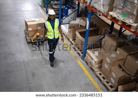Young man pulling hand pallet truck loading package boxes stacked in shipping warehouse. Multiracial worker move merchandise from godown shelf by hand lift pallet jack. Delivery goods, cargo transport Royalty-Free Stock Photo #2336485151