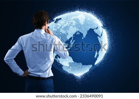Back view of thoughtful young businnessman looking at glowing globe hologram on blurry blue background. Digital earth and metaverse concept