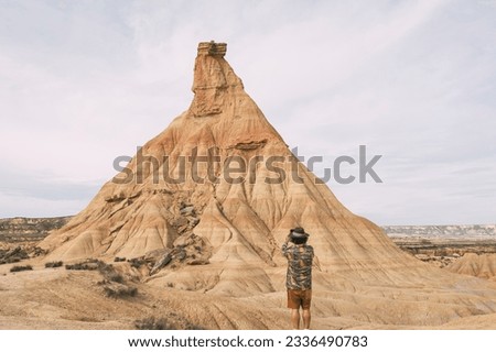 Rear View Of A Man With A Hat Taking A Photo With A Smart Phone In The Bardenas Desert. Navarre