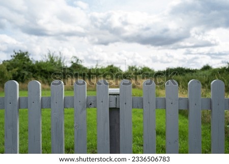 Shallow focus of a recently painted wooden fence seen boarding a private garden with a distant grassy meadow.