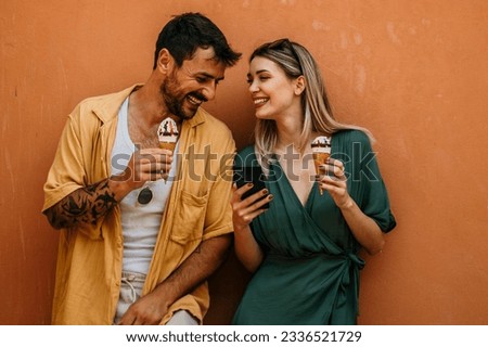 A young tourist couple laughs as they share a large ice cream sundae, making the most of their day together in the city. Royalty-Free Stock Photo #2336521729