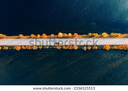 Aerial view of fall road and blue water lake sea ocean. Red car with a roof rack on a country road in Finland. Beautiful autumn landscape in FInland.