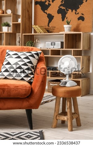 Interior of stylish living room with sofa and electric fan on stool Royalty-Free Stock Photo #2336538437