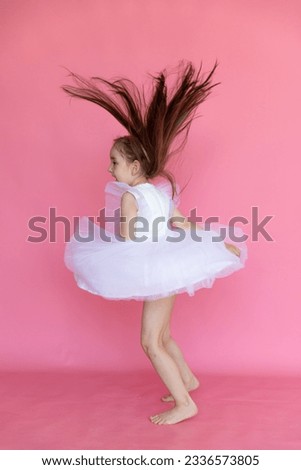 Rear view of little girl in a pink princess dress has fun and jumping on pink background. Kids Birthday party celebration concept. Happy Birthday banner with copy space. Studio shot.