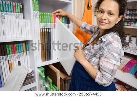 Gorgeous multiethnic pregnant woman with big belly, inspired art teacher painter taking out canvas from the shelf, smiling looking at camera standing in a creative art store. Hobby. Art class. People