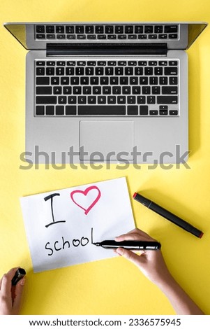 I love school the child's hand writes in a paper on a yellow background.
