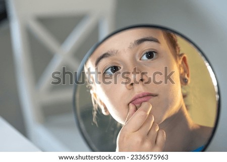 A teenage girl looks thoughtfully at her reflection in the mirror.