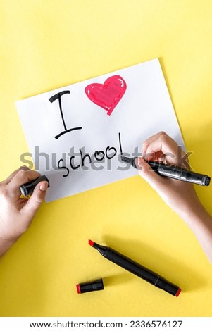I love school the child's hand writes in a paper on a yellow background.