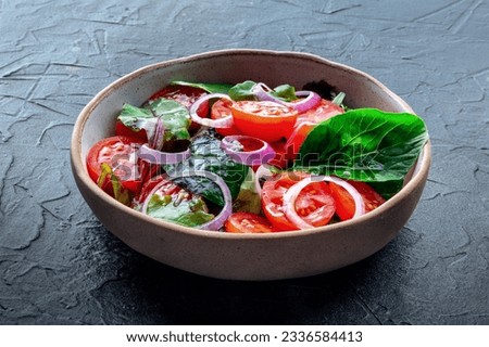 Salad with tomato, fresh leaves, and onions, on a black slate background. Healthy diet, simple vegan recipe