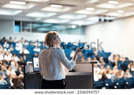 Female speaker giving a talk on corporate business conference. Unrecognizable people in audience at conference hall. Business and Entrepreneurship event Royalty-Free Stock Photo #2336594757