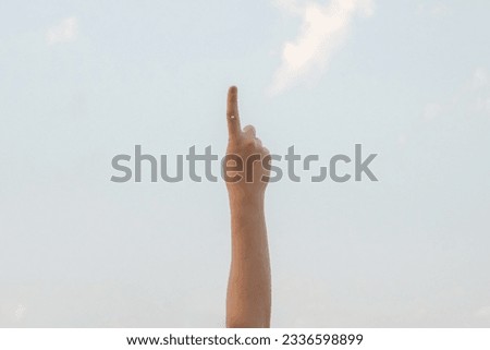Hand doing, showing number one gesture symbol on bright blue summer sky nature background. Gesturing number 1. Number one in sign language. First and counting one concepts. 1 finger up