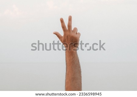 Hand doing, showing number three gesture symbol on bright blue summer sky nature background. Gesturing number 3. Number three in sign language. Third and counting three concepts. 3 finger up Royalty-Free Stock Photo #2336598945