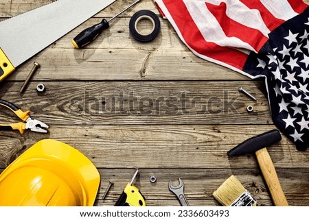Happy Labor day concept. Frame made of carpentry tools, safety helmet, American flag on wooden desk table. Flat lay, top view.