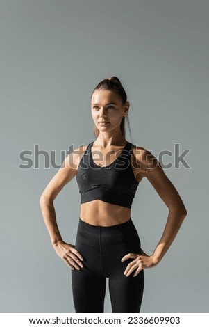 fit sportswoman in sports bra and leggings holding hands on hips and looking away isolated on grey Royalty-Free Stock Photo #2336609903