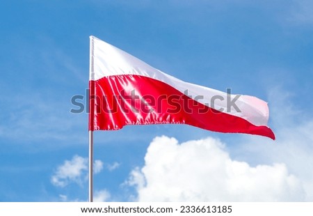 The flag of Poland is a rectangular cloth divided into two equal horizontal halves - white and red against a blue sky during a summer day