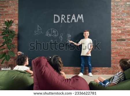 Little boy, child standing at black and drawing his dreamings about being musician. Imagination. Psychology and creative thinking. Concept of school, education, childhood, knowledge, lifestyle