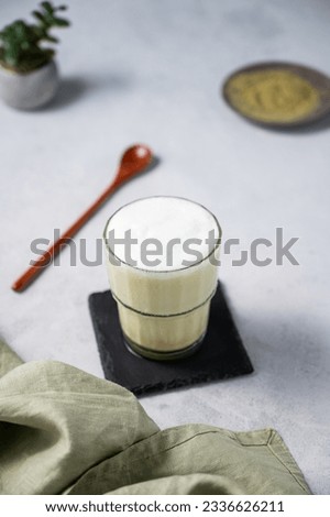 Matcha latte with ice. Green tea with milk in a glass on a light background with spoon, napkin. The concept of a traditional healthy Japanese summer refreshing drink. Top view.