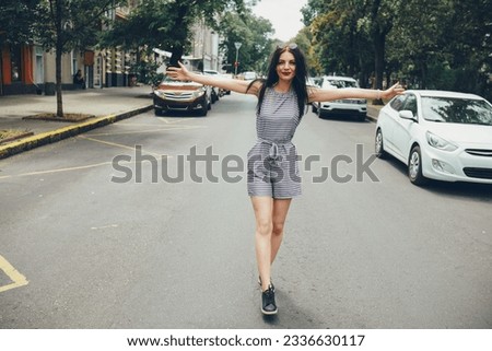 A happy girl walks down the street along the roadway with her arms outstretched and smiling. Royalty-Free Stock Photo #2336630117