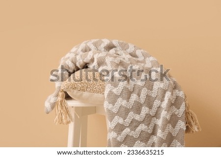 Stool with cushion and cozy blanket near beige wall