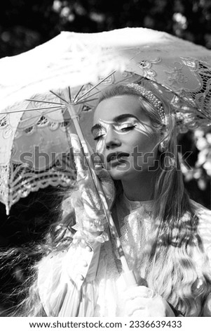 Long-haired blonde with a vintage umbrella posing in a blooming apple park. Black and white photo