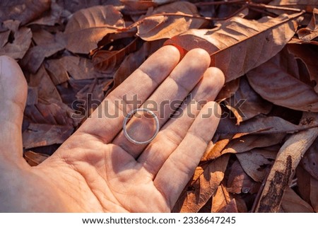Wedding ring photo shoot concept man hold wedding ring with sun light and dry leaf background. The photo is suitable to use for wedding invitation photo background and wedding content media.