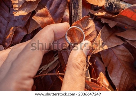 Wedding ring photo shoot concept man hold wedding ring with sun light and dry leaf background. The photo is suitable to use for wedding invitation photo background and wedding content media.