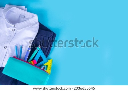 Preparation for school, back to school background. School children's student uniform, skirt, pants, shirt with pencil case, study accessories on bright blue background top view flatlay copy space