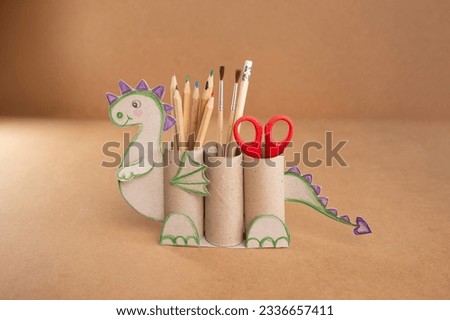 dragon shape a pencil holder made out of toilet paper and a pair of scissors, educational and craft activity Royalty-Free Stock Photo #2336657411