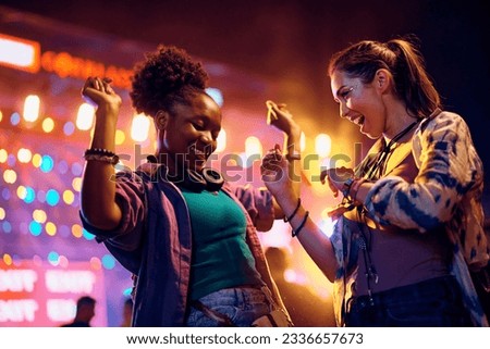 Happy African American woman and her female friend having fun and dancing while attending open air music concert at night. Royalty-Free Stock Photo #2336657673