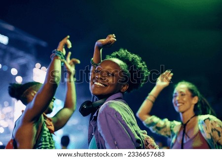 Happy African American woman dancing with her friends at open air music concert at night and looking at camera. 