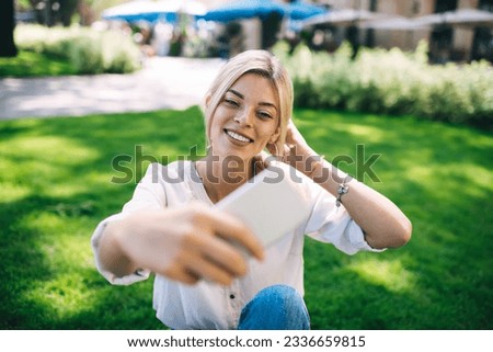Cheerful female vlogger spending leisure in park for shooting video content for sharing in social media, happy hipster girl posing while clicking selfie photo images on cellular technology