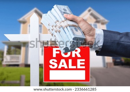 Buyer Handing Over Cash for House with Home and For Sale Real Estate Sign Behind