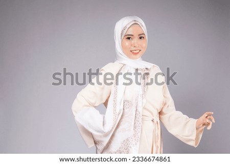 A portrait of young smiling muslim woman wearing a hijab over plain background studio.