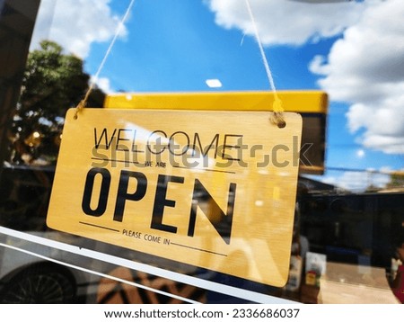 Wooden sign mounted on glass door Write a message in black ink "Welcome we are open please come in". The sign is installed in front of the restaurant, coffee shops. Text on vintage wooden sign
